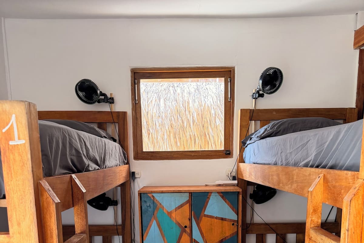 A bunk bed room with a window, a wooden cabinet with geometric patterns, and a wooden floor.