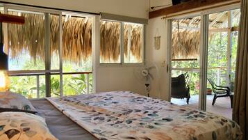 Un dormitorio con una cama, un ventilador y ventanas grandes con tejados de paja.