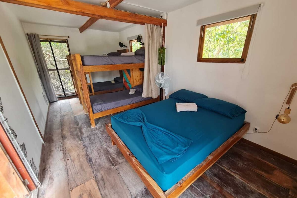 A room with a bunk bed, a single bed, a fan, a window, and a telephone.