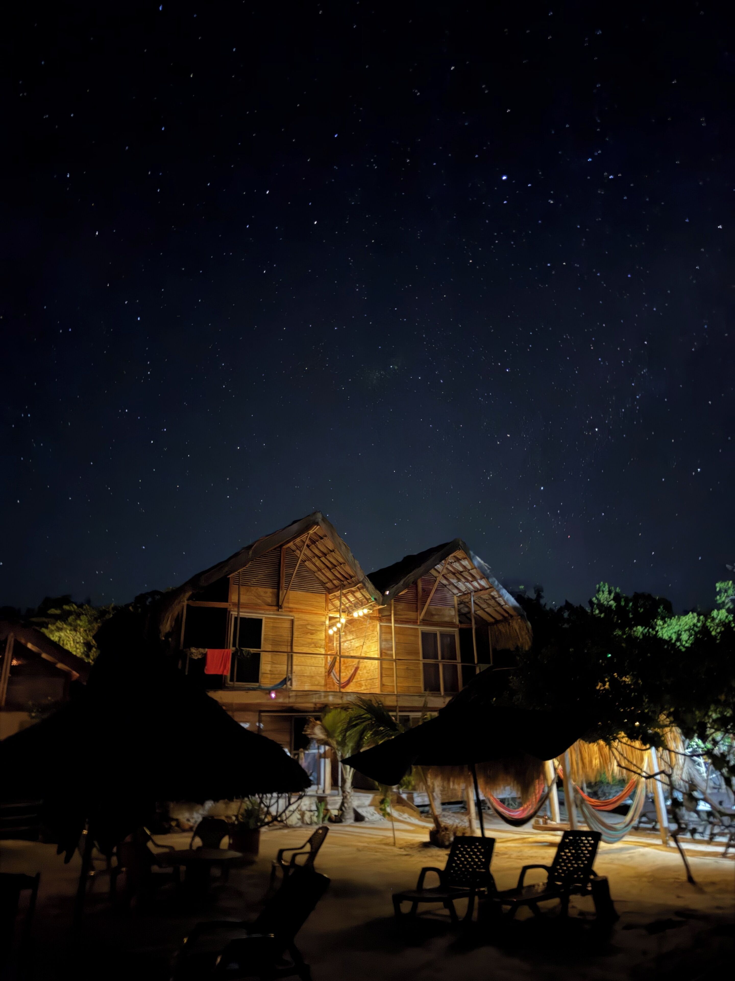 Una propiedad frente al mar con un edificio de techo de paja, asientos exteriores y un cielo estrellado.