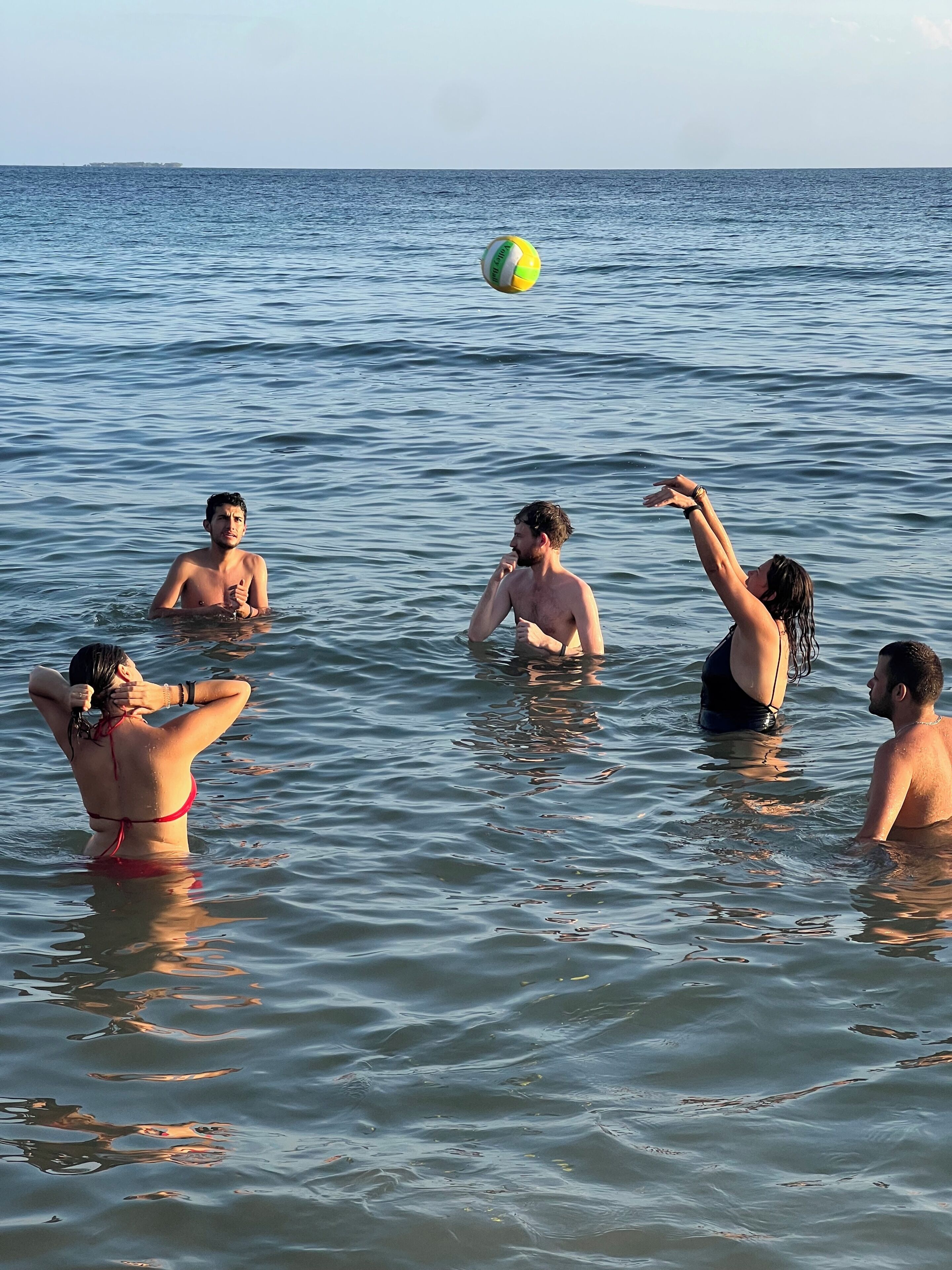 Een groep mensen in het water, waarschijnlijk op een strand of meer, met een volleybal.