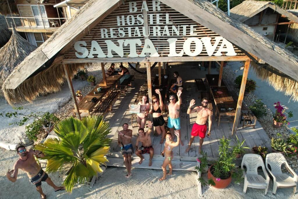 A beachside bar, hostel, and restaurant named 'Santa Iova' with a thatched roof and outdoor seating.