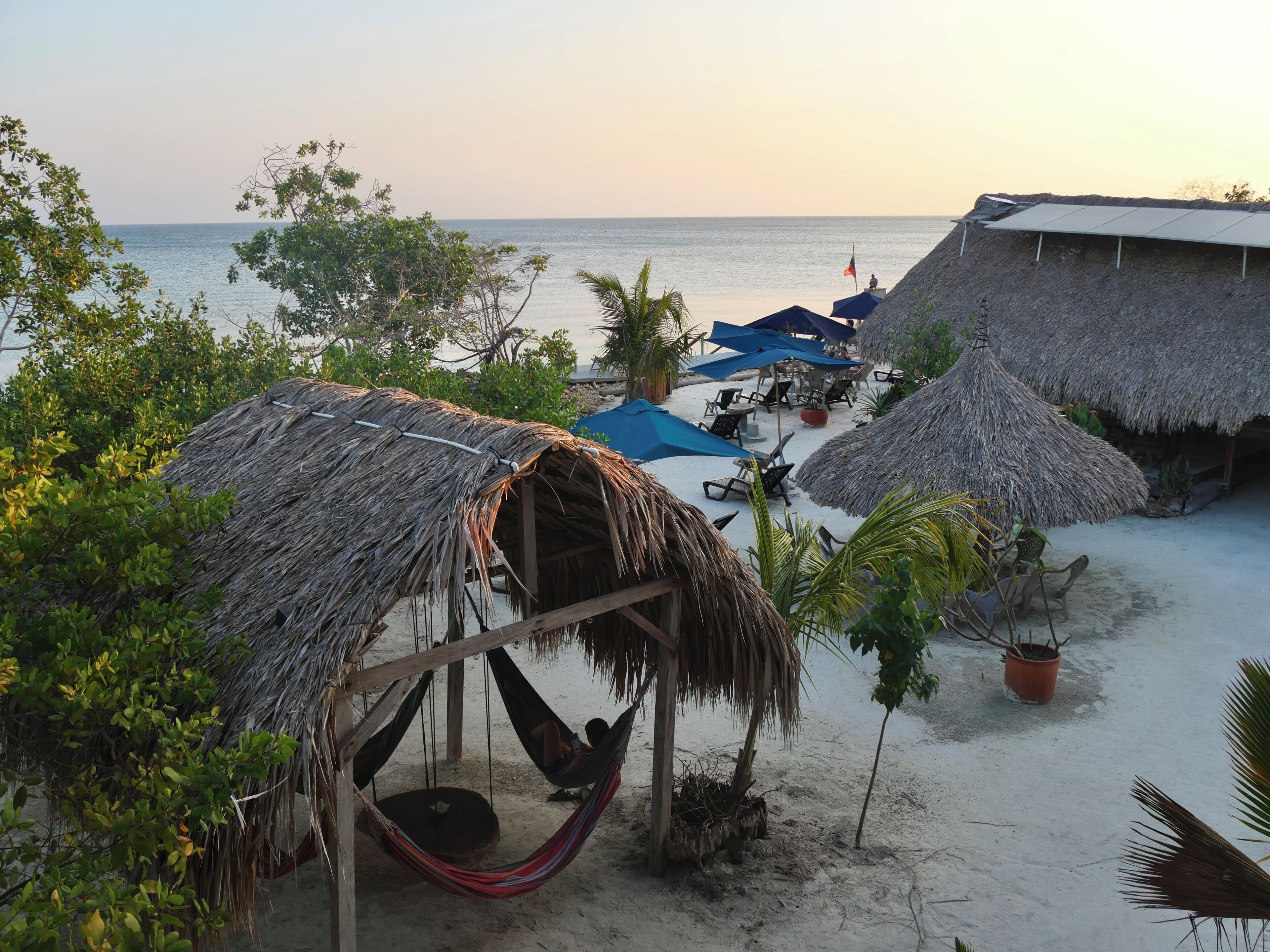 Eine Strandlandschaft mit strohgedeckten Hütten, einer Hängematte und Liegestühlen.