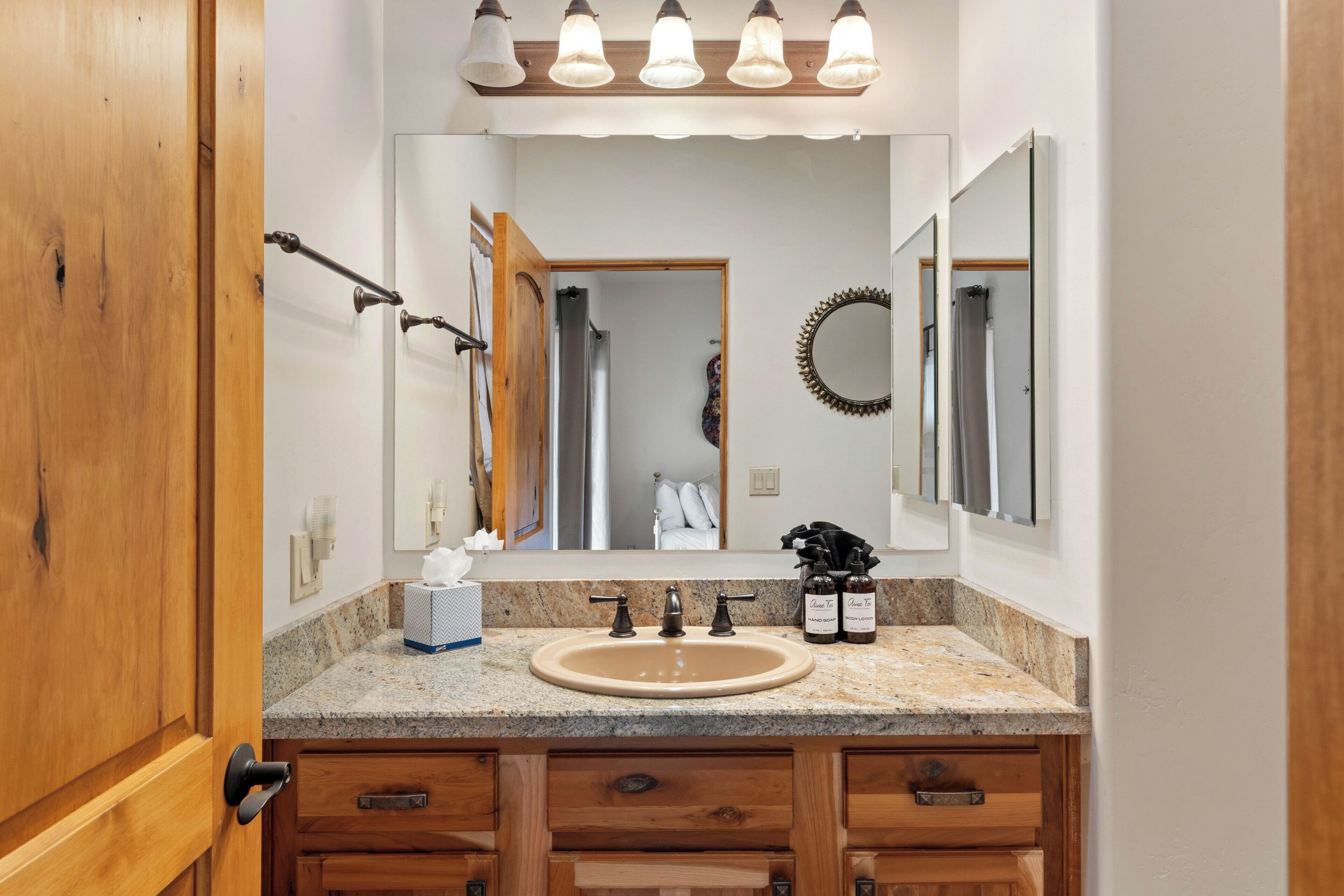 Une salle de bain avec un comptoir en granit, un lavabo, un miroir et des armoires en bois.