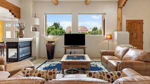Ein Wohnzimmer mit Fernseher, Ledersofa und einem großen Fenster mit Blick auf rote Felsformationen.