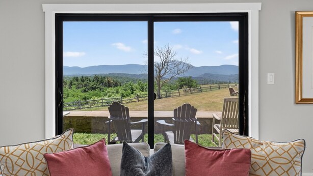 Une pièce dotée d’une grande porte-fenêtre coulissante qui donne sur un patio extérieur aménagé avec des fauteuils Adirondack et offrant une vue sur un paysage montagneux.