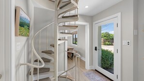 Un escalier en colimaçon avec une main courante, une porte donnant sur l’extérieur et un tableau encadré accroché au mur.