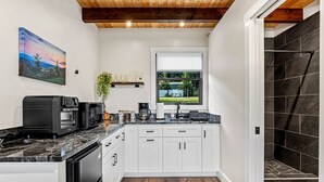 A modern kitchen with white cabinets, a black refrigerator, and a window with a view of greenery. - Hot Tub Outdoor Movies Firepit Mtn Views (Mills River)
