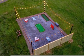 An aerial view of a fenced outdoor area with a putting green, a small pool, and a shuffleboard table. - Hot Tub Outdoor Movies Firepit Mtn Views (Mills River)