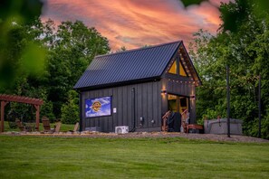 A small, dark wooden building with a sloped roof and a large illuminated sign. - Hot Tub Outdoor Movies Firepit Mtn Views (Mills River)