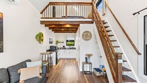 A spacious living area with a high ceiling, a wooden staircase, and a kitchen in the background. - Hot Tub Outdoor Movies Firepit Mtn Views (Mills River)