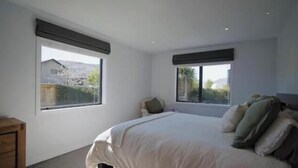A bedroom with a bed, two windows, a nightstand, and a dresser. - Near new 4 bed 2 Bath House in Hanleys Farm, Queenstown (Jacks Point)