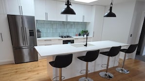 A modern kitchen with a central island, stainless steel appliances, and black bar stools. - Near new 4 bed 2 Bath House in Hanleys Farm, Queenstown (Jacks Point)