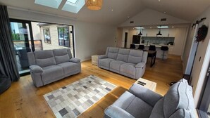 A spacious living area with two grey sofas, a patterned rug, and a kitchen in the background. - Near new 4 bed 2 Bath House in Hanleys Farm, Queenstown (Jacks Point)