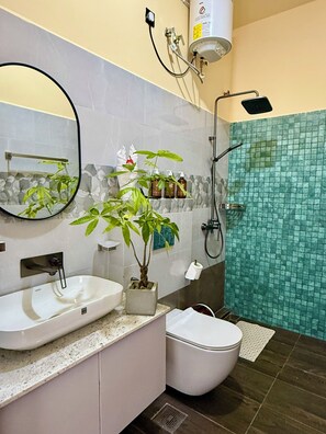 A bathroom with a white sink, a toilet, a shower, a mirror, and a potted plant.