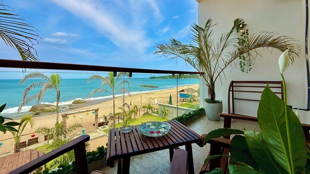 A balcony with a view of the beach, a table with a bowl, and potted plants.