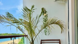A balcony with a potted plant, wooden furniture, and a view of the beach.