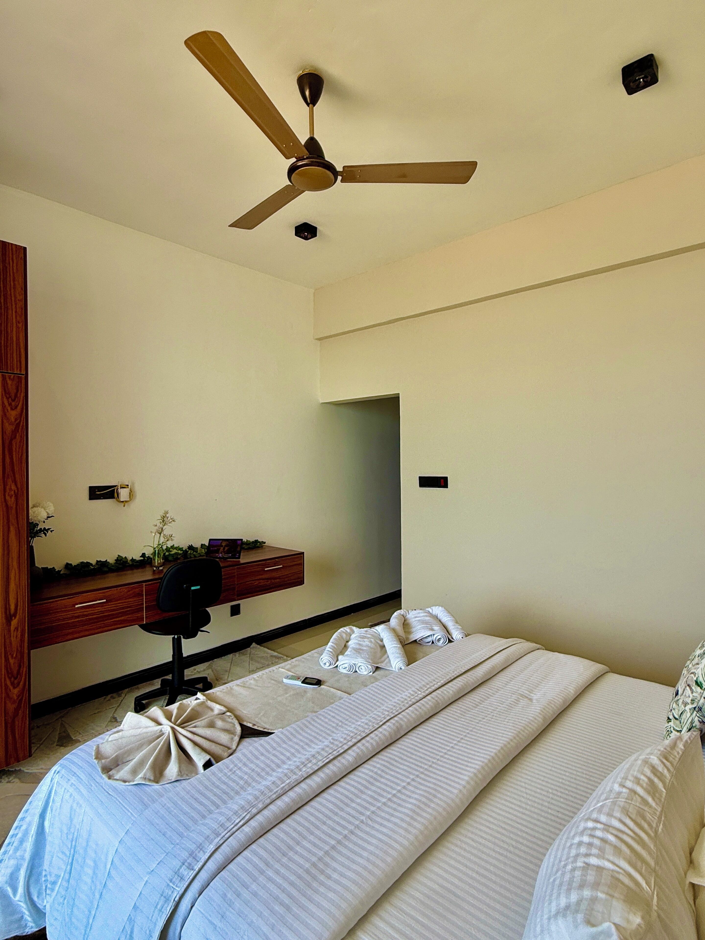 Hotelkamer met een bed, bureau, stoel, plafondventilator en spiegel.