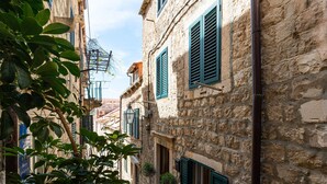A narrow street with stone buildings, green shutters, and potted plants. - Villa Jele (Dubrovnik)