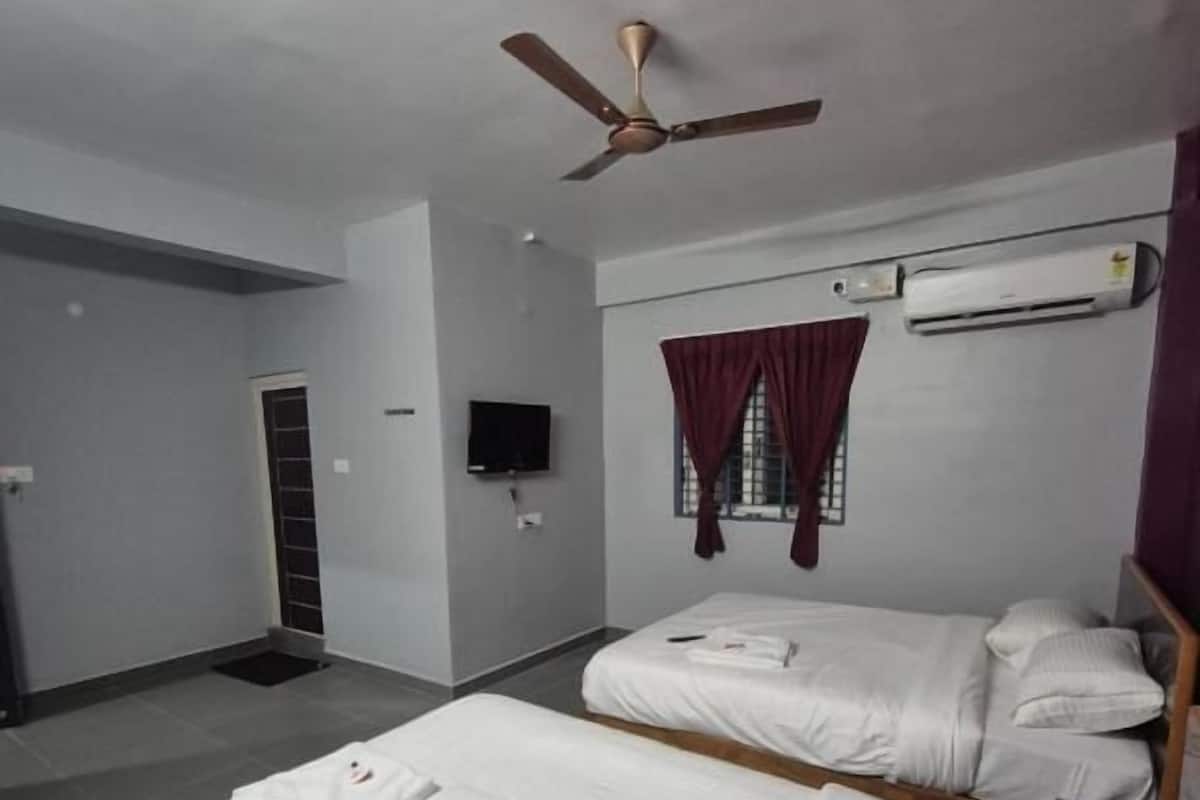 Une chambre d’hôtel avec deux lits, un ventilateur de plafond, un appareil de climatisation, une télévision et une fenêtre avec des rideaux.