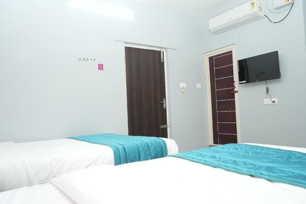 A hotel room with two beds, a television, an air conditioning unit, and a door.
