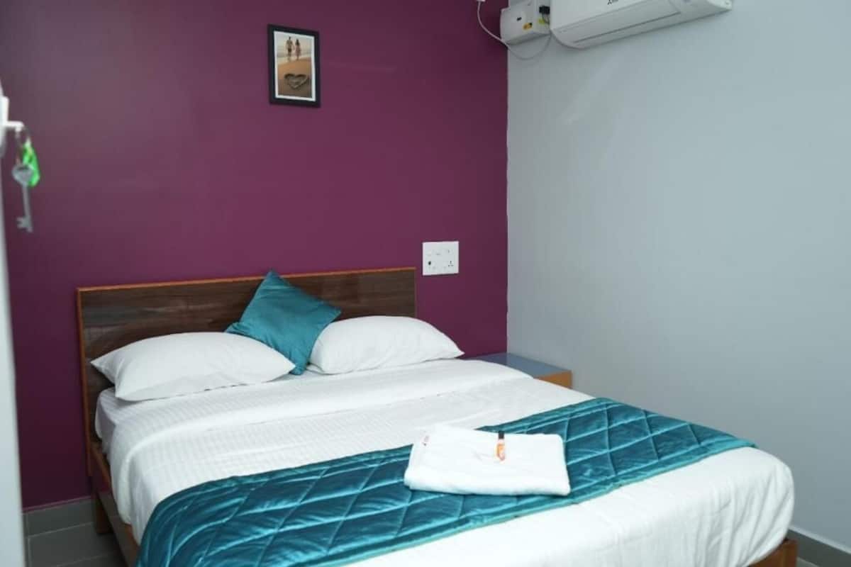 Un lit simple avec une tête de lit en bois, du linge de lit blanc et une couverture matelassée de couleur turquoise.