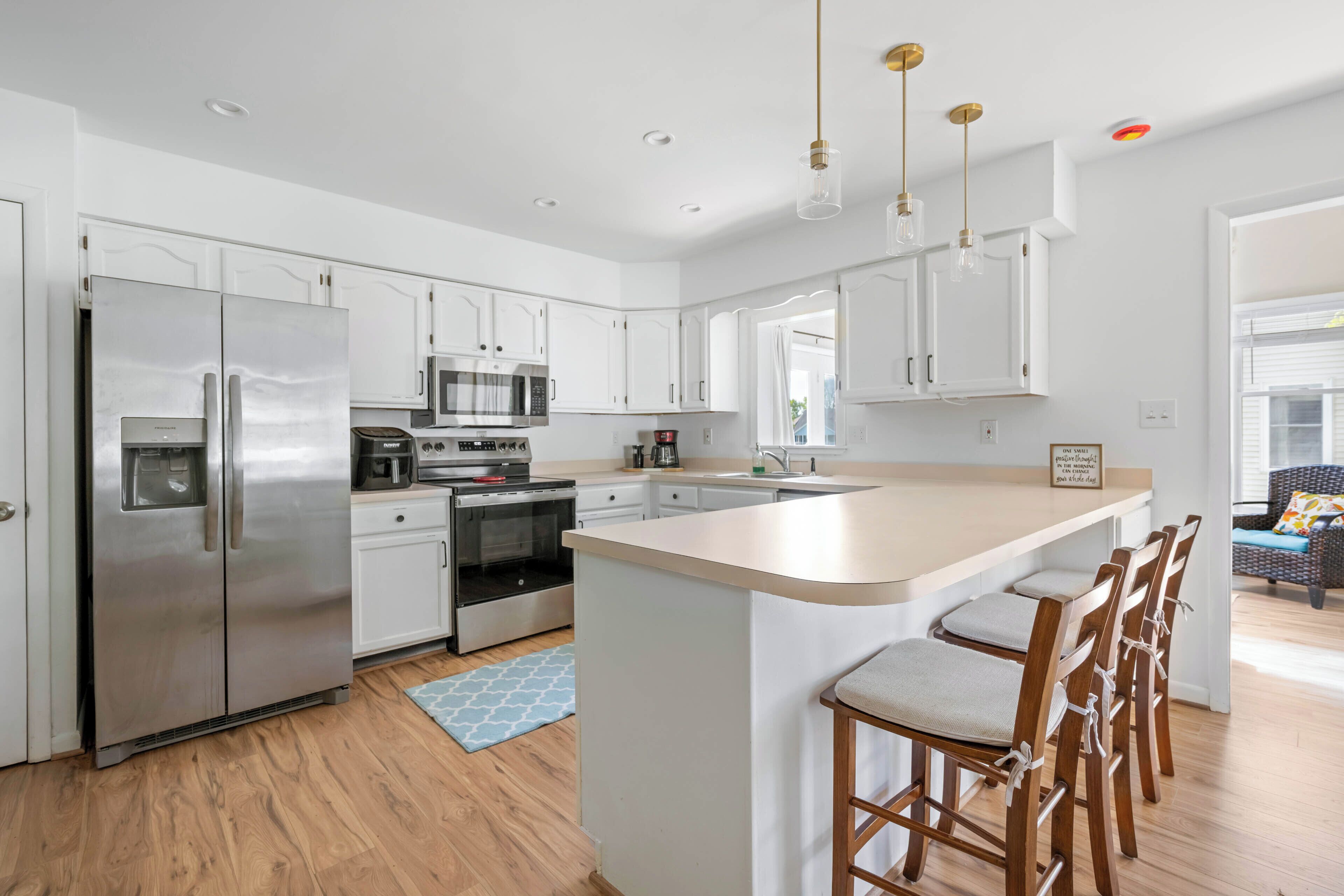 A modern kitchen with stainless steel appliances, white cabinetry, a central island with bar stools, and a blue patterned rug.