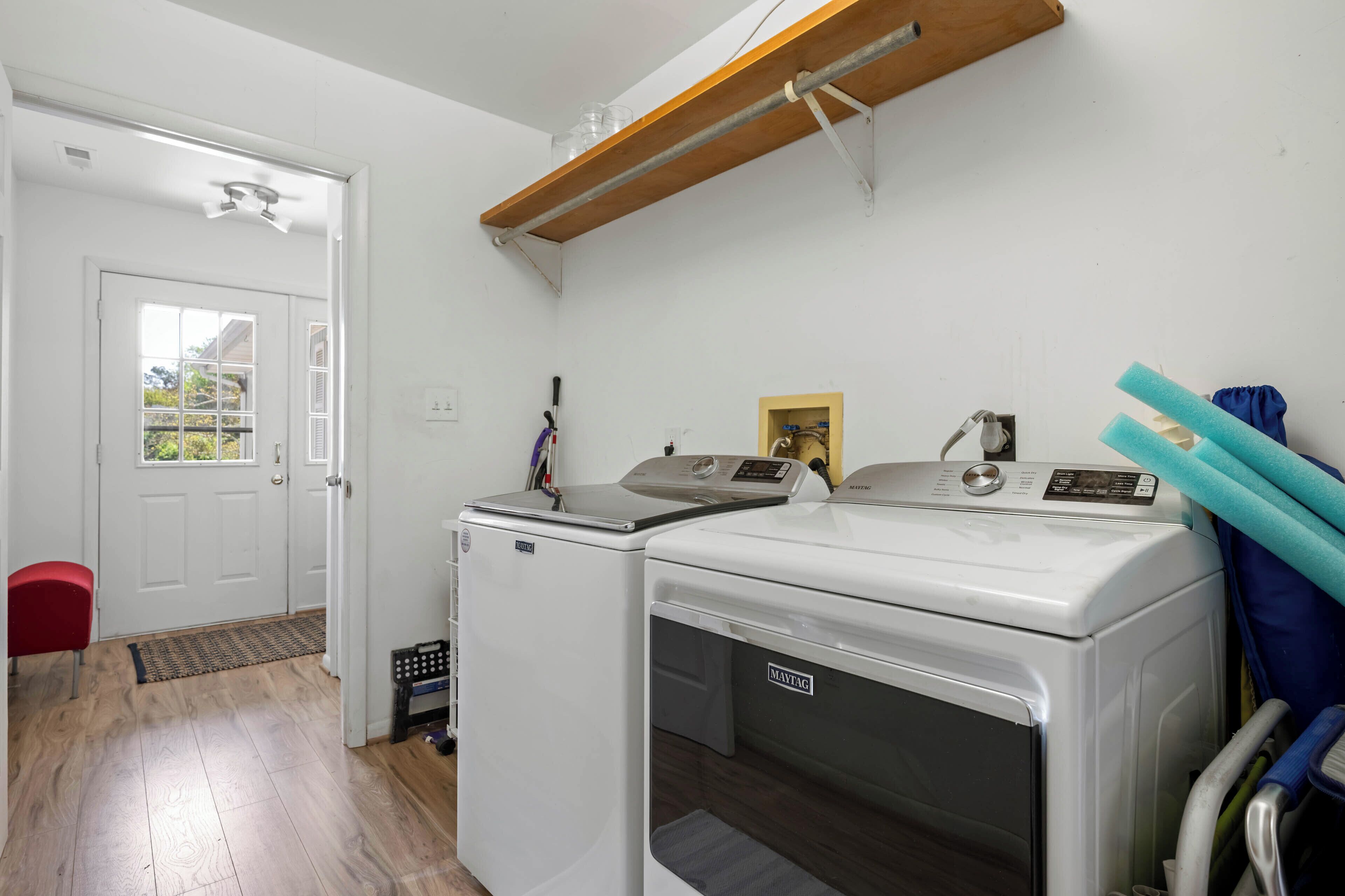 A laundry room with two washing machines, a red chair, and a wooden shelf above.