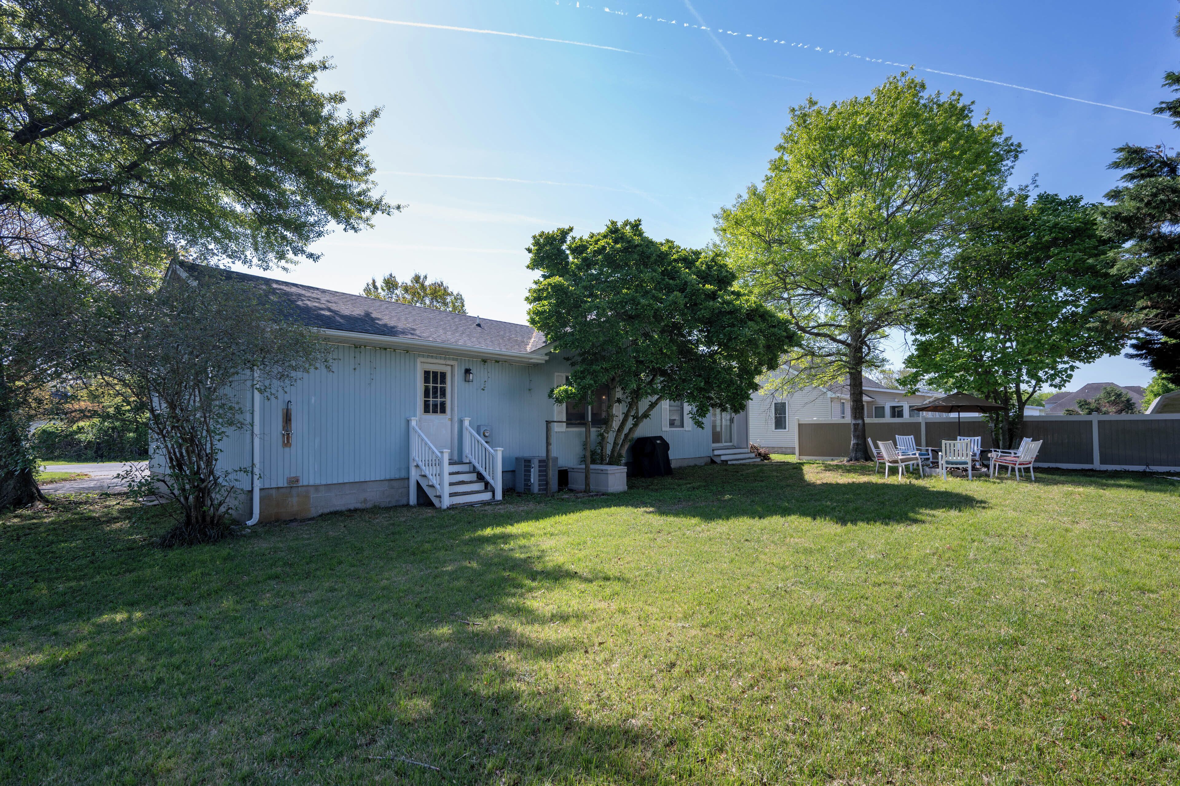 A single-story house with a front porch, a small yard, and a patio with outdoor furniture.