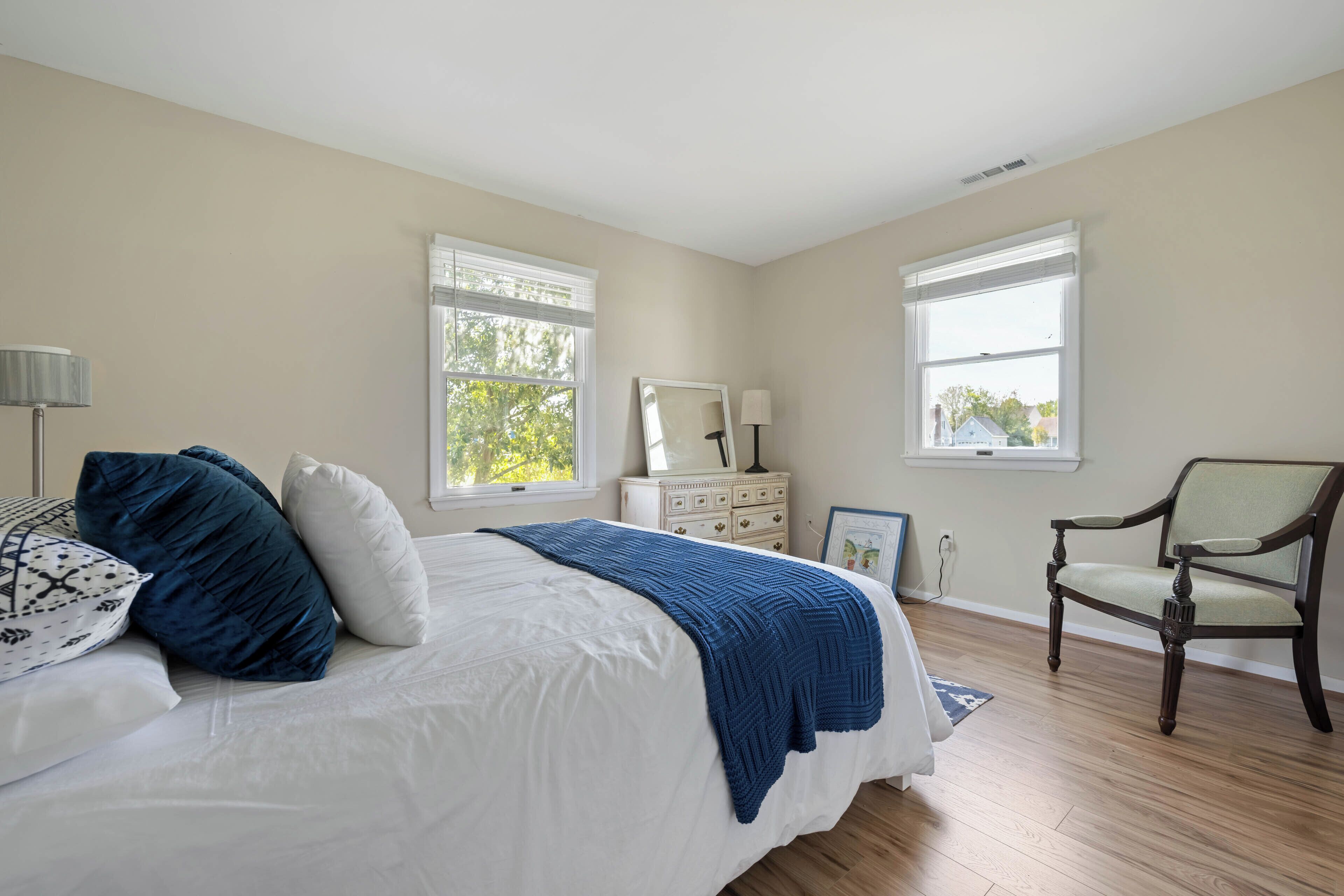 A bedroom with a bed, dresser, chair, and two windows.