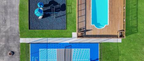 Vista aérea de un complejo de piscinas con una zona de buceo separada, una terraza de madera y una cancha de tenis.