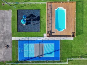 Vue aérienne d’un complexe de piscines comprenant une zone distincte pour les plongeons, une terrasse en bois et un court de tennis.