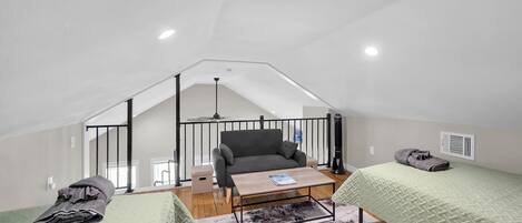 Un dormitorio tipo loft con techo inclinado, un sofá, una mesa de centro y dos camas.