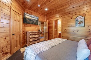 A wooden cabin interior with a bed, a mounted television, and a fireplace. - Gatlinburg Mountain Lodge 5 Bedroom Cabin (Gatlinburg)