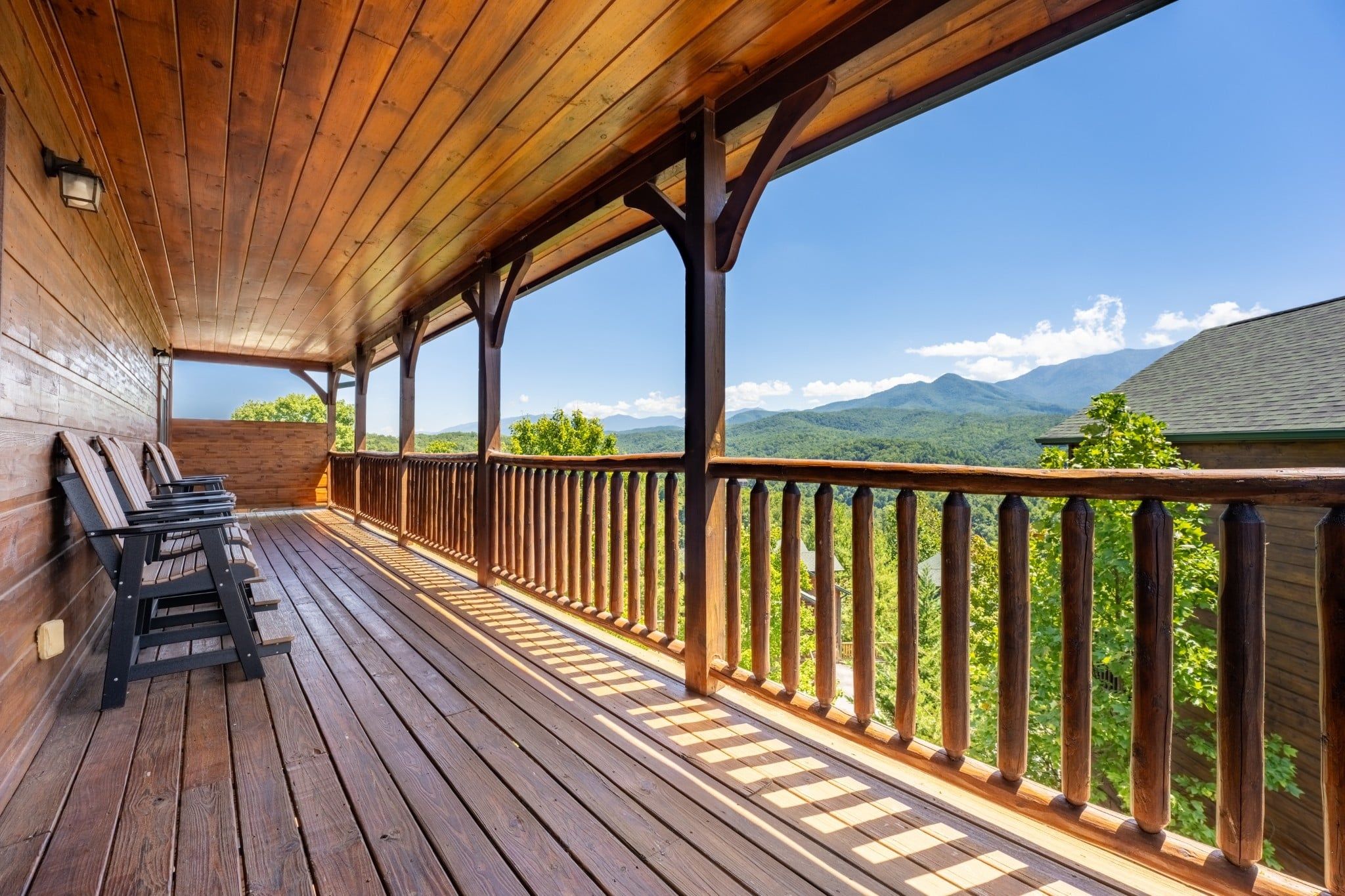 A wooden deck with a railing, a bench, and a view of mountains.