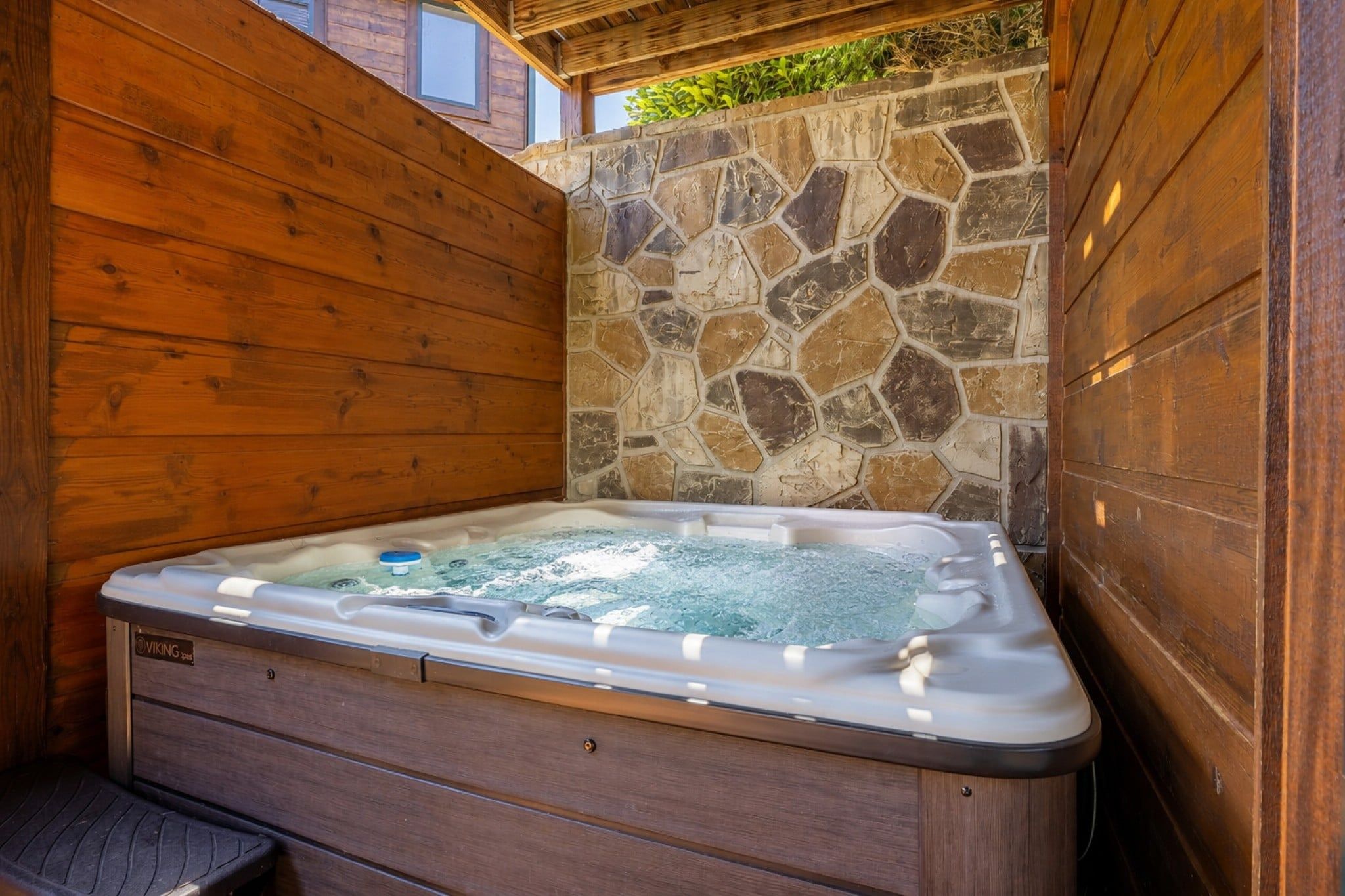 Un bain à remous avec un mur en pierre et des panneaux en bois.