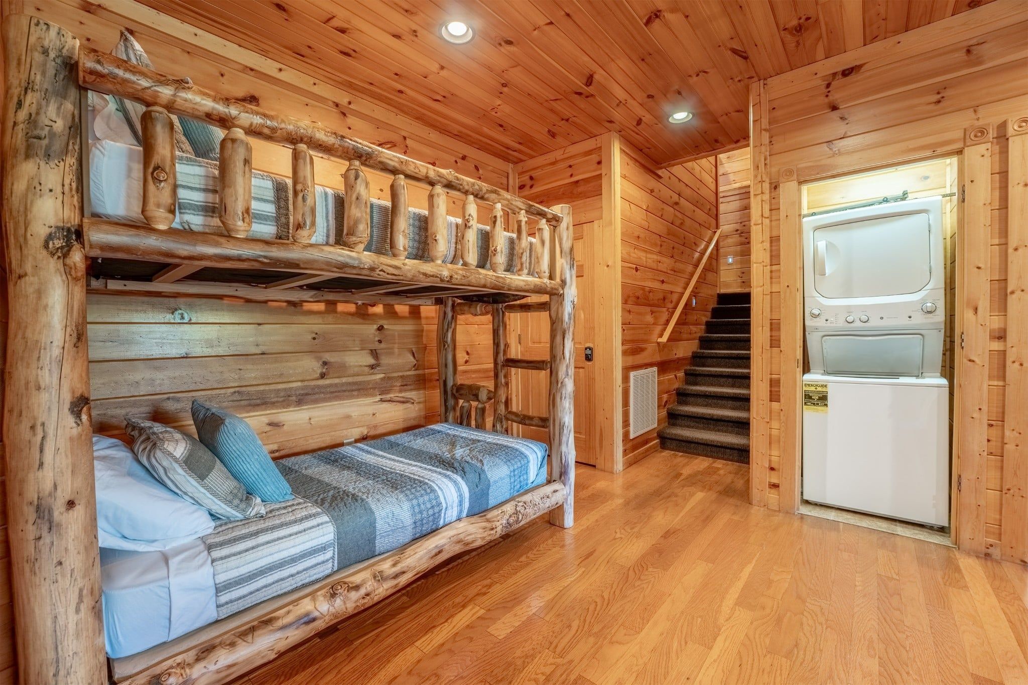 A wooden interior with a bunk bed, a washing machine, and a staircase.