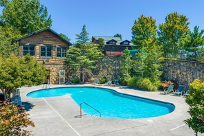 A swimming pool with a stone wall and lounge chairs. - Gatlinburg Mountain Lodge 5 Bedroom Cabin (Gatlinburg)