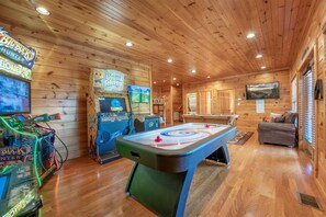 A wooden interior with a pool table, arcade games, and a television. - Gatlinburg Mountain Lodge 5 Bedroom Cabin (Gatlinburg)