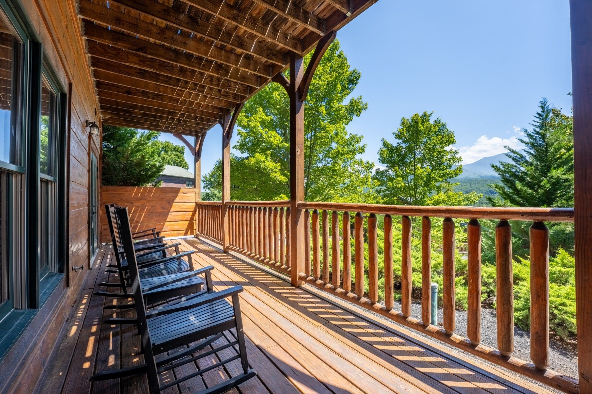 A wooden deck with chairs and a railing overlooking a forested landscape.