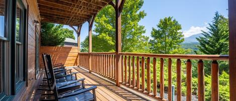 A wooden deck with chairs and a railing overlooking a forested landscape.