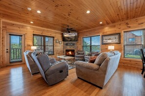 A cozy cabin interior with wooden walls, a fireplace, and a seating area with two sofas and two armchairs. - Gatlinburg Mountain Lodge 5 Bedroom Cabin (Gatlinburg)