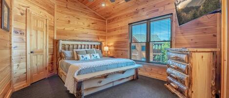 A wooden cabin bedroom with a bed, a ceiling fan, a window with blinds, and a log cabinet.