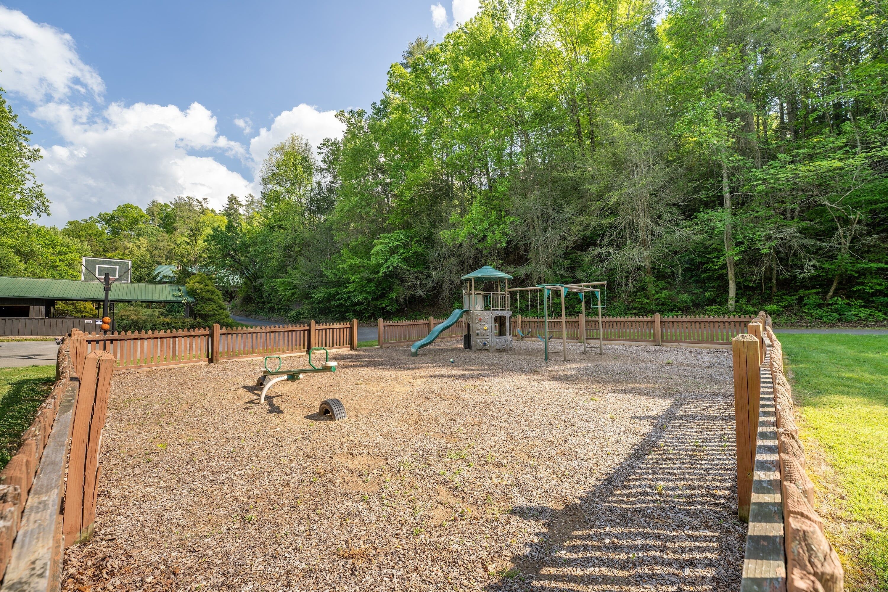 A playground with a slide, climbing structures, and a basketball hoop.
