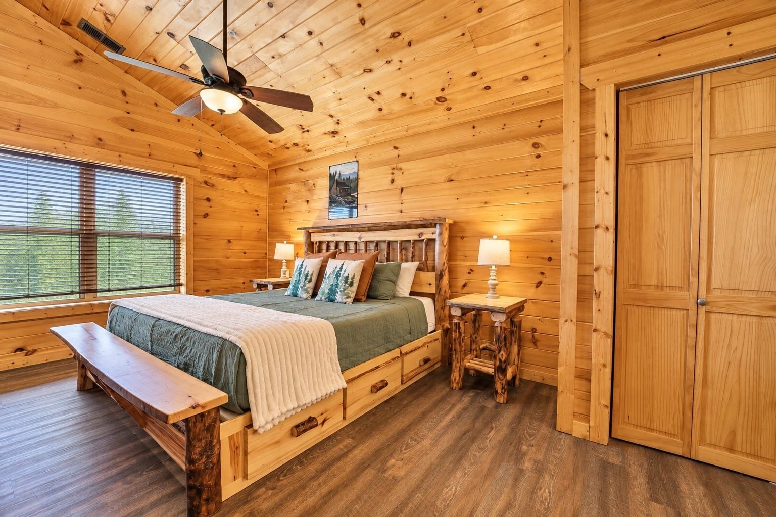 Une chambre aménagée dans un chalet en rondins, avec un lit, un banc, un ventilateur de plafond et une grande porte en bois.
