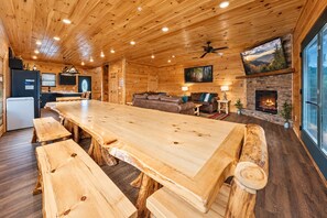 A log cabin interior with a long wooden dining table, a fireplace, and a stone wall. - Gatlinburg Views Lodge 5 Bedroom Cabin (Gatlinburg)