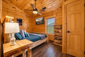 A wooden cabin room with a bed, a table, a lamp, a ceiling fan, a window with blinds, and a door. - Gatlinburg Views Lodge 5 Bedroom Cabin (Gatlinburg)