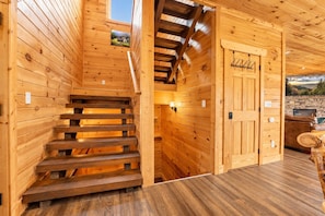 Ein Holzinnenraum mit einer Treppe zu einem Erkerbereich, einer Holztür mit Wappen und einer Steinwand mit einem Fernseher.