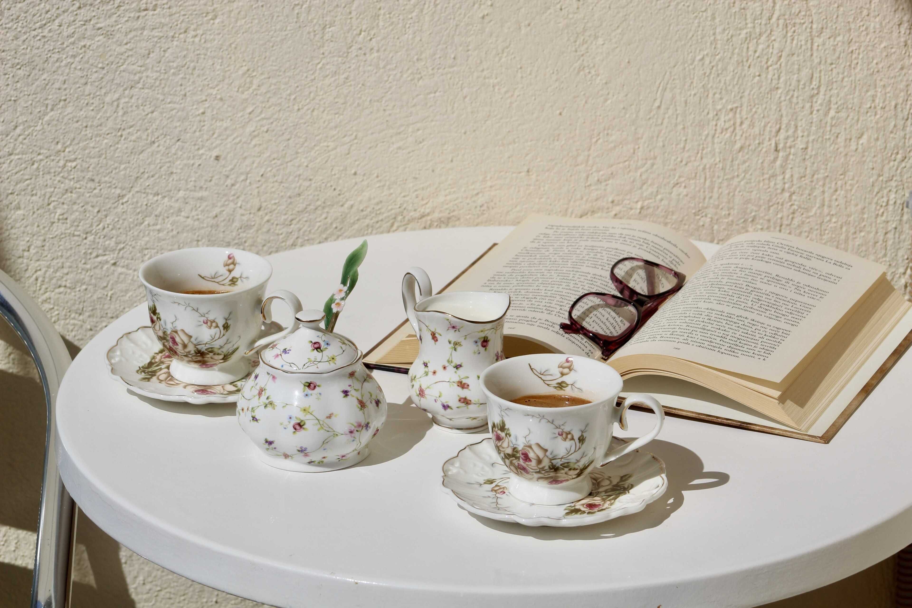 Uma mesa branca com chávena, chá, um livro e copos.