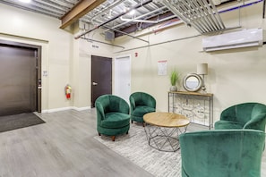 A lobby with a reception desk, two green armchairs, a round wooden table, and a fire extinguisher.